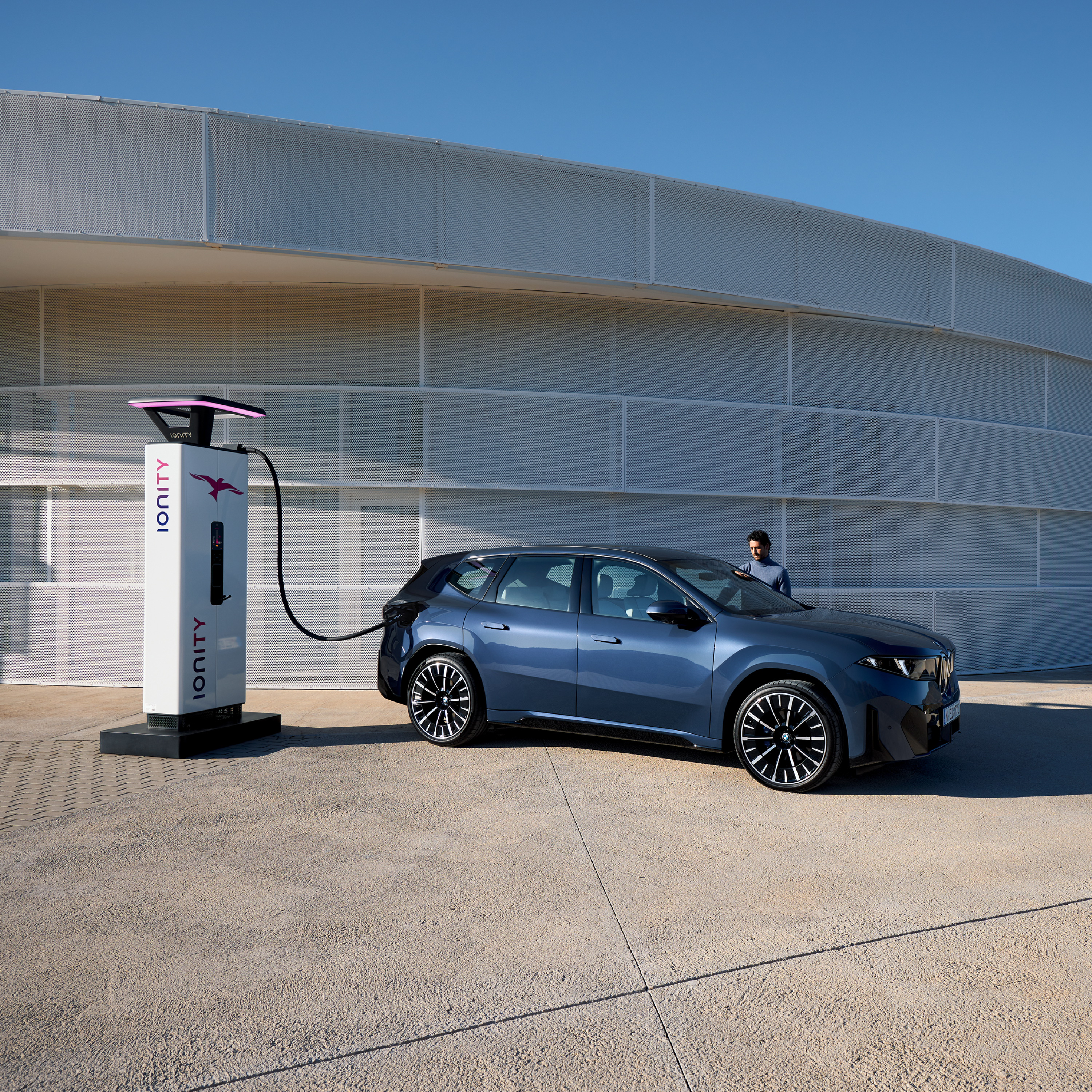 Ein Mann steht neben einem BMW iX3, der an einer öffentlichen Ladesäule angeschlossen ist